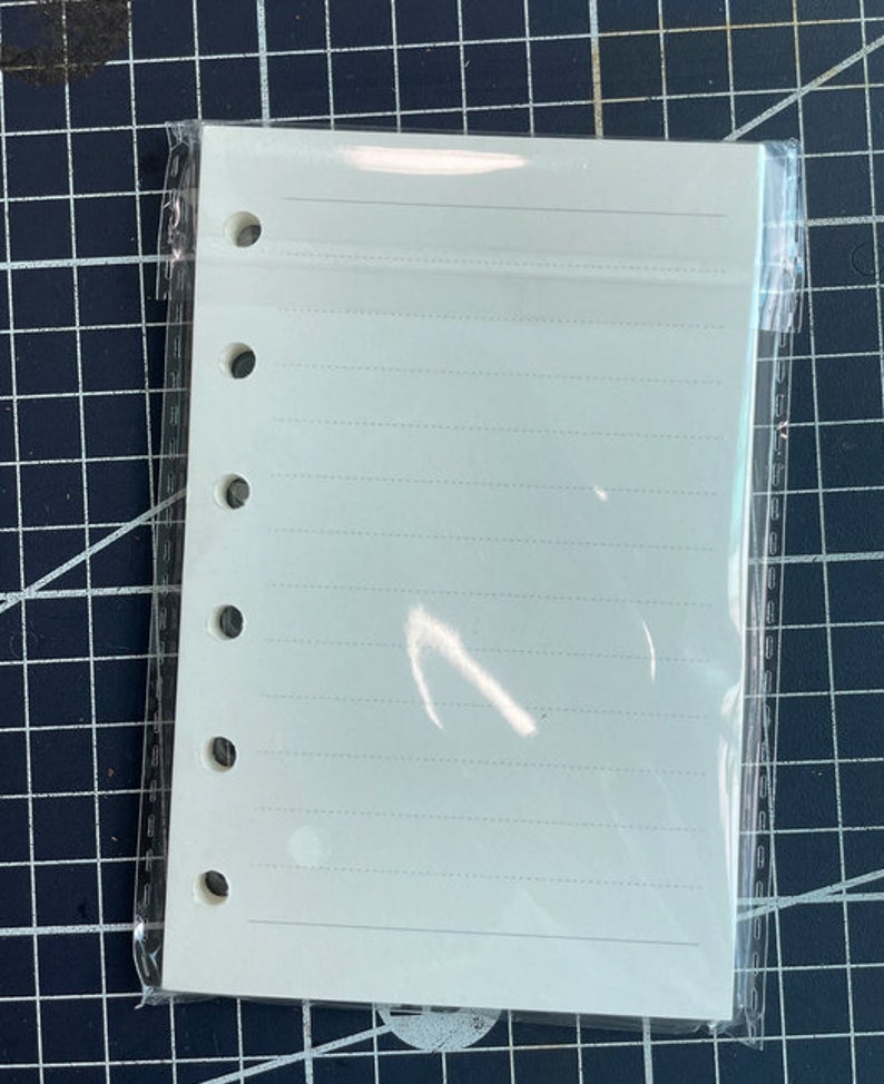 May include: A white, lined, paper refill for a 6-ring binder. The paper is packaged in a clear plastic sleeve.