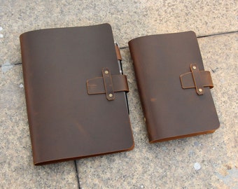 May include: Two brown leather journals with a distressed look. The larger journal has a strap closure with brass accents. The smaller journal has a similar strap closure.
