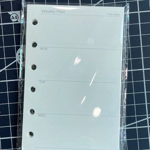 May include: A white weekly planner with a plastic cover. The planner has six lines for each day of the week, starting with Monday and ending with Wednesday. The planner has the text "Weekly Plan" at the top and "This week" at the top right.