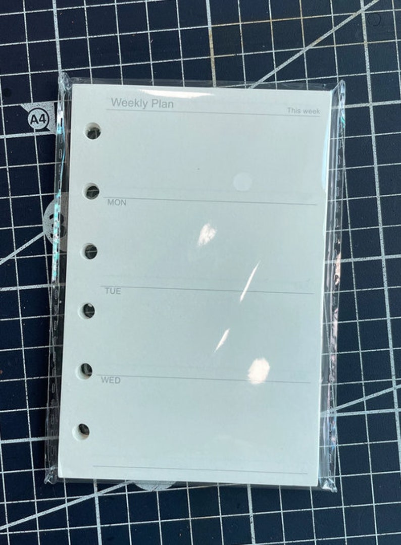 May include: A white weekly planner with a plastic cover. The planner has six lines for each day of the week, starting with Monday and ending with Wednesday. The planner has the text "Weekly Plan" at the top and "This week" at the top right.