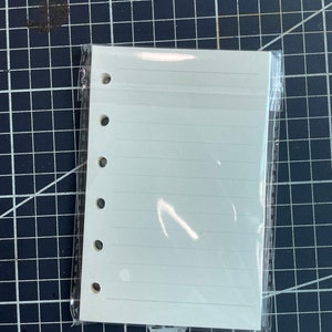 May include: A white, lined, blank notebook with a clear plastic cover and six holes down the side for a binder.