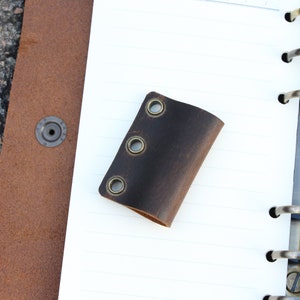 May include: A brown leather notebook page holder with three brass eyelets.