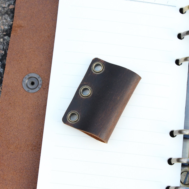 May include: A brown leather notebook page holder with three brass eyelets.