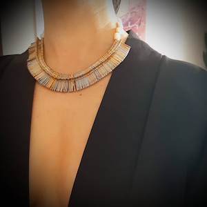 Peut inclure: Un collier superposé or et argent avec un design en frange. Le collier est porté par une personne avec un blazer noir.