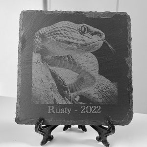 May include: A black and white engraved slate plaque with a close-up image of a snake's head and the text "Rusty - 2022".