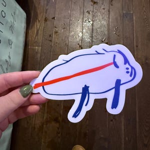 May include: A white sticker with a blue outline of a pig with a red line across its body. The pig is lying on its side with its legs in the air.