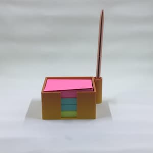 May include: Orange desk organizer with a pen holder and a stack of pink, blue, and green sticky notes.