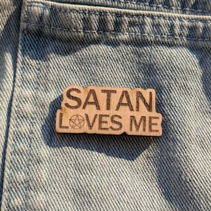 Peut inclure: Une épingle en bois avec le texte "SATAN LOVES ME" et un symbole de pentagramme.