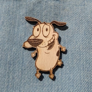 May include: A wooden cutout of the cartoon character Courage the Cowardly Dog. The cutout is brown and features Courage's signature wide eyes and goofy grin.
