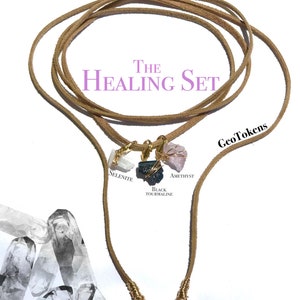 K&ouml;nnte beinhalten: Das Healing Set von GeoTokens besteht aus einem braunen Lederband mit vier Kristallanh&auml;ngern: Selenit, Amethyst, schwarzer Turmalin und einem vierten Kristall. Das Band ist an den Enden mit Golddraht umwickelt.