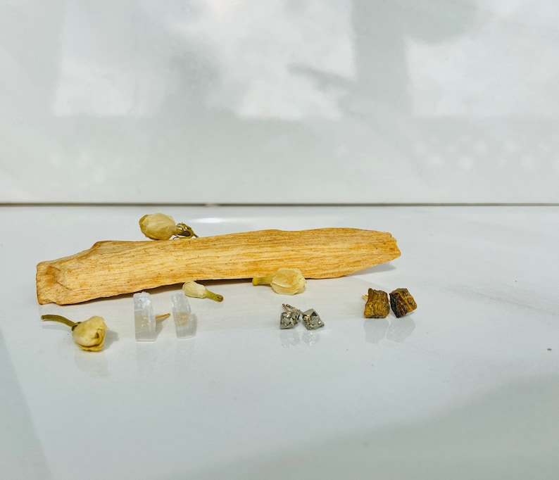 May include: A piece of natural wood with white flowers and small silver and brown square-shaped earrings on a white surface.