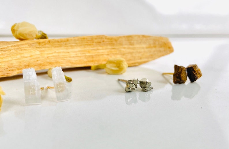 May include: Three pairs of earrings with different crystal styles. The first pair is white, the second pair is silver, and the third pair is brown.