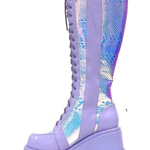 May include: A knee-high platform boot in light purple with a thick, lugged sole. The boot features a lace-up front with matching purple laces and panels of iridescent, holographic material with a snakeskin-like texture along the shaft.