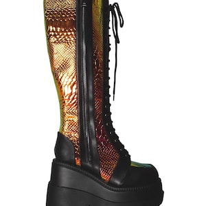 May include: A knee-high platform boot featuring a black matte base with a thick, lugged sole. The upper combines black panels with iridescent, metallic gold and copper snakeskin-textured material, finished with black laces and a side zipper.