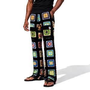 May include: Full-length trousers constructed from a black crochet fabric featuring a repeating granny square pattern in vibrant colors including yellow, blue, red, and green. The pants include a black waistband and two front patch pockets.