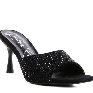 May include: A black mule sandal featuring a square toe, a flared kitten heel, and a wide strap across the front covered in small black rhinestones. The insole displays the white script text London Rag, providing a clear view of the shoe design.
