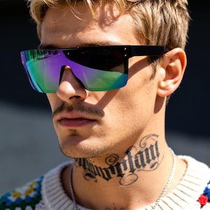 May include: Shield sunglasses featuring a flat-top black frame and a single continuous lens with a reflective, iridescent purple and green gradient finish. The design includes two small silver-toned rivets on each side of the frame near the temples.