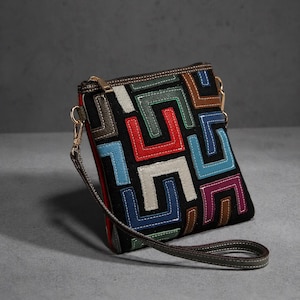 May include: A black square crossbody bag featuring a geometric pattern of U-shaped leather patches in red, blue, light blue, purple, green, brown, and cream. The bag includes a top zipper closure, gold-tone metal hardware, and a detachable wrist strap.