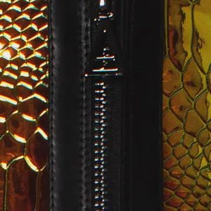 May include: A black zipper with a triangular metal pull tab centered between two panels of iridescent, metallic gold and copper material featuring a textured, repeating scale pattern that reflects light across the surface of the object.