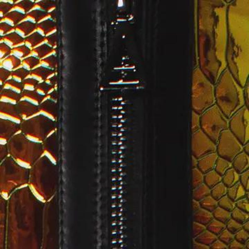 May include: A black zipper with a triangular metal pull tab centered between two panels of iridescent, metallic gold and copper material featuring a textured, repeating scale pattern that reflects light across the surface of the object.