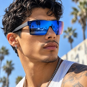 May include: Shield sunglasses featuring a single continuous lens with a reflective blue mirror finish and a matte black frame. The design includes a flat top bar and integrated side arms, providing a wide field of vision and a sleek, modern appearance.