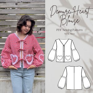 May include: A sewing pattern for a blouse with a heart detail. The pattern is called "Demure Heart Blouse" and is available in sizes XS to XL. The pattern is shown on a white background with a model wearing a red and white gingham blouse.