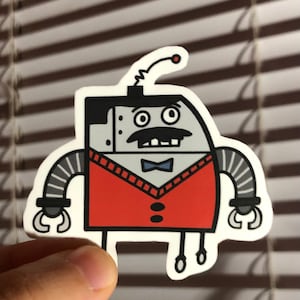 May include: A sticker featuring a cartoon robot with a mustache, bow tie, and red vest. The robot has a gray body, black hair, and striped arms. The robot's arms end in claw-like hands. The sticker has a white border.