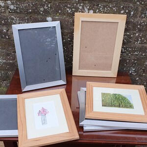 May include: A collection of picture frames in various sizes and styles. Some frames are silver, while others are wood. The frames are arranged on a wooden table.