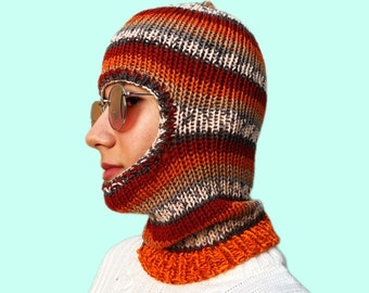 May include: A striped knitted balaclava with orange, brown, and gray stripes. The balaclava has a face opening and a neck opening.