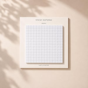 Op de afbeelding: Een vierkant memoblok met een wit ruitjespatroon. Het blok is bevestigd op een crèmekleurige achterkaart met de tekst STICKY NOTEPAD bovenaan, het woord GRAPH eronder en FAYE CO PAPIER onderaan op de kaart gedrukt.