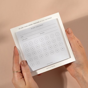 Op de afbeelding: Een witte sticky notepad met een 30-daagse challenge tracker. De notepad heeft ruimte voor een doel, een startdatum en een einddatum. De tracker is een raster met 30 cirkels, genummerd van 1 tot en met 30. De notepad is gelabeld "Faye Co Papier".