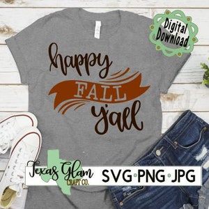 Puede incluir: Una camiseta gris con el texto "happy fall y'all" en letras negras y marrones. La camiseta está sobre una superficie de madera con un par de zapatillas blancas y unos pantalones cortos de mezclilla azul.