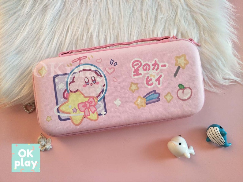 Puede incluir: Estuche de transporte rosa para Nintendo Switch con un personaje de dibujos animados de Kirby en una nave espacial. El estuche tiene un texto japon&eacute;s que dice "Space Kirby".