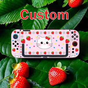 May include: A pink handheld gaming console with a custom design featuring a white cat face, strawberries, and floral accents. The word "Custom" is displayed in red. The console is set against a backdrop of green leaves and fresh strawberries.