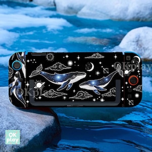 Könnte beinhalten: Schwarze Nintendo Switch Konsolen-Hülle mit einem himmlischen Wal-Design. Die Hülle hat einen schwarzen Hintergrund mit weißen Wolken, Sternen und Monden. Die Wale haben ein Galaxie-Design. Der Text "OK play" ist sichtbar.