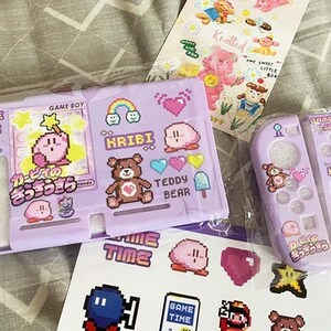 May include: A purple and pink Nintendo Switch game case with a pink Kirby character design. The case has a matching controller skin with a pink Kirby character design. The case and controller skin have the text "Game Time" and "Kribbi" on them.