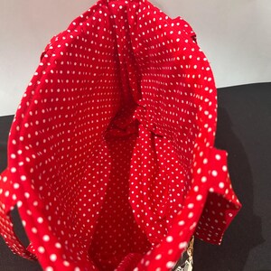 May include: A fabric tote bag featuring a vibrant red interior lining with a white polka dot pattern. The bag has two matching red and white polka dot fabric handles attached to the sides, with a glimpse of a patterned exterior visible at the base.