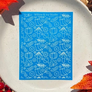 May include: A blue sheet with a white pattern of autumn-themed illustrations, including pumpkins, mushrooms, leaves, and boots. The text "Willow & Ivy Studio" is at the top of the sheet.