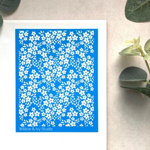 May include: A blue stencil with a white floral pattern. The stencil is rectangular and has the text "Willow & Ivy Studio" at the bottom.