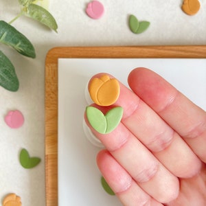 May include: A set of two polymer clay flower charms. One charm is a yellow tulip and the other is a green leaf.
