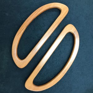 Op de afbeelding: Twee ovale handvatten voor een handtas van hout. De handvatten zijn lichtbruin van kleur met een gladde afwerking. De handvatten zijn gemaakt van hout en zijn ontworpen om aan een handtas of tas te worden bevestigd.