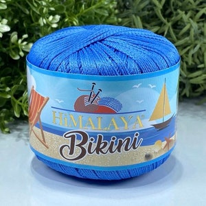 May include: A ball of bright blue yarn wrapped in a paper label featuring the text HiMALAYA Bikini, an illustration of a beach scene with a sailboat, a lounge chair, and a graphic of yarn balls with knitting needles on a sandy shore.