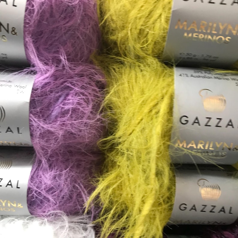 Puede incluir: Dos ovillos de hilo, uno morado y otro amarillo. El hilo es peludo y tiene una textura suave. El hilo est&aacute; etiquetado como "GAZZAL MARILYN MERINOS".