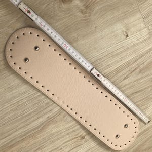 Puede incluir: Una correa de cuero beige con múltiples agujeros espaciados uniformemente y ojales de metal plateado. La correa mide 76 cm de largo.