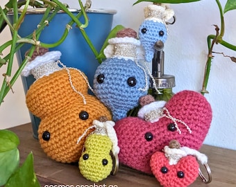 May include: Five crocheted amigurumi keychains in the shape of bottles and hearts. The bottles are in shades of blue and orange, and the hearts are red and pink. The keychains are all attached to silver key rings.