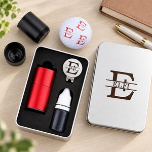 Può includere: Un set regalo da golf composto da una pallina da golf bianca con una lettera E rossa e il nome ELFI, una scatola di metallo argentato con lo stesso monogramma, un timbro cilindrico rosso, un flacone di inchiostro nero e un segnapalla circolare.