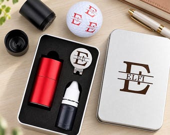 May include: A golf gift set featuring a white golf ball with a red letter E and the name ELFI, a silver metal tin with the same monogram, a red cylindrical stamp, a small black ink bottle, and a silver circular ball marker with the letter E and ELFI.