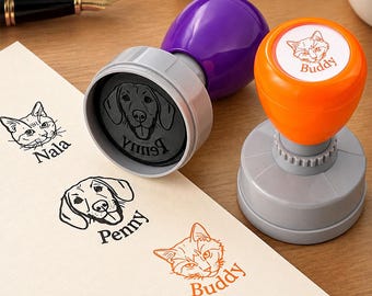 May include: Two round self-inking stamps with purple and orange handles. The purple stamp features a dog face and the name Penny. The orange stamp features a cat face and the name Buddy. Stamped impressions of a cat named Nala, a dog named Penny, and a cat named Buddy appear on the paper.