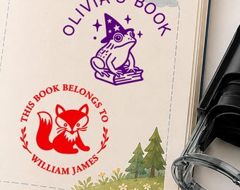 May include: Two ink stamps on a page. One purple stamp shows a frog wearing a wizard hat sitting on a book with the text OLIVIA'S BOOK. One red stamp shows a fox inside a circular frame with the text THIS BOOK BELONGS TO WILLIAM JAMES.