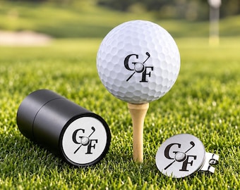 May include: A white dimpled golf ball on a wooden tee, a black cylindrical container, and a silver metal golf ball marker. Each item features a black logo with the letters GF and a small golf ball graphic integrated into the letter G.